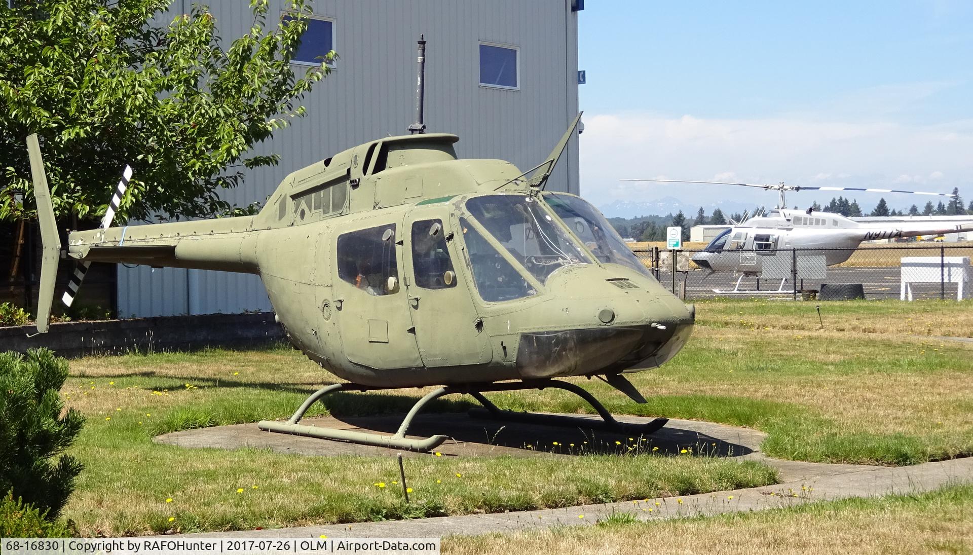68-16830, 1968 Bell OH-58A Kiowa C/N 40144, The OH-58 is 68-16830, The OH-58A Kiowa, engine and rotor-less and without markings or identification with, in the background, a visitor from the State of Arkansaw OH-58A N911A.