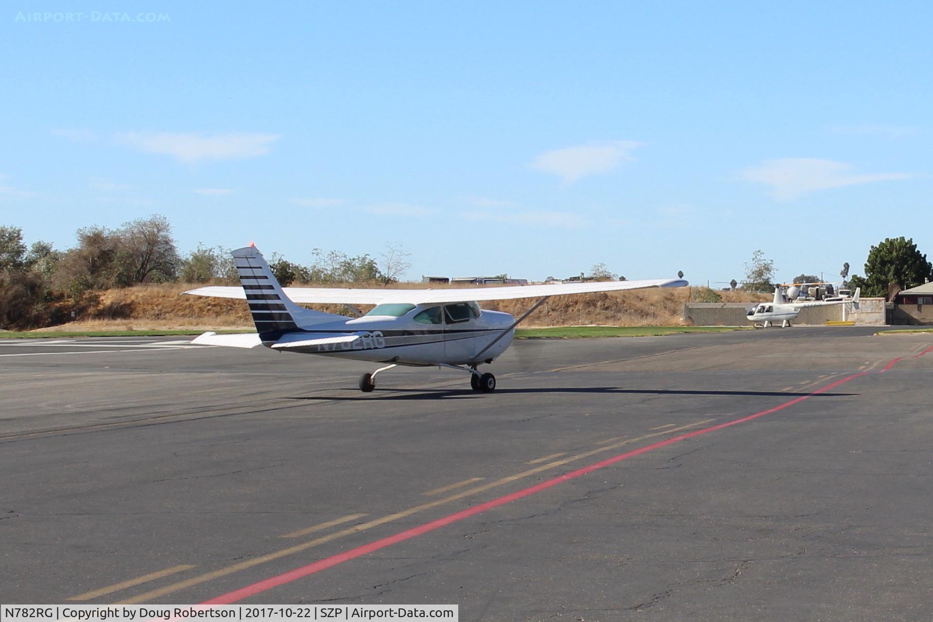N782RG, 1978 Cessna R182 Skylane RG C/N R18200194, 1978 Cessna R182 SKYLANE RG, Lycoming O-540 235 Hp, holding short Rwy 04. Note N544DL Robinson R44 Helo in background near its hangar, will fly today.