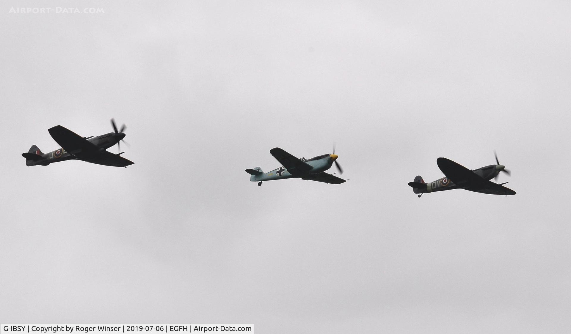 G-IBSY, 1942 Supermarine 349 Spitfire Vc C/N EE602, Three Ultimate Warbirds with Spitfire G-IBSY (Coded DV-V) over Runway 04 leading Buchon G-AWHM (coded Yellow 7) and Spitfire G-SPIT (coded JE-J).