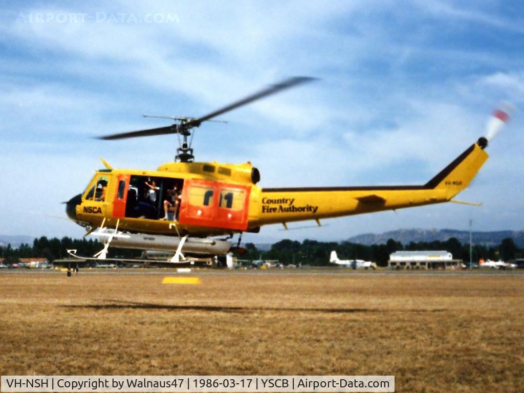VH-NSH, 1975 Bell 205A-1 C/N 30195, Low res Port side view of hovering NSCA Bell 205A-1 VH-NSH Cn 30195 Code 01 at Canberra Airport YSCB on 17Mar1986. This Helo wears a 'Country Fire Authority' logo and is equipped with a water tank and filler hose, for Fire-fighting duties