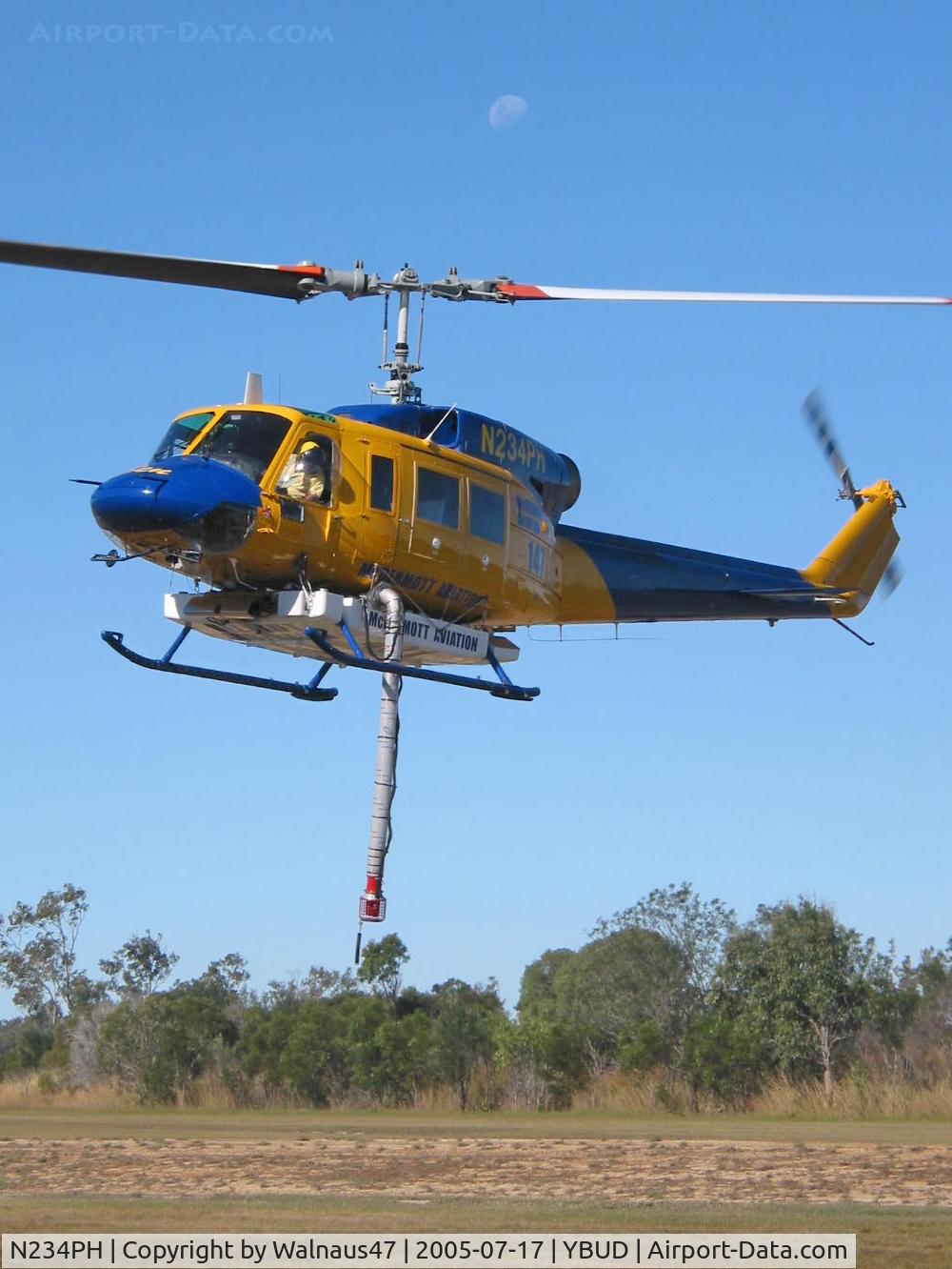 N234PH, 1977 Bell 214B-1 Biglifter C/N 28050, Front Portside view of McDermott Aviation Bell 214B-1 Biglifter N234PH Cn 28050 hovering at Bundaberg Airshow at Bundaberg Airport YBUD on 17Jul2005. Equipped with ‘under-cabin’ water tank, with ‘pick-up’ hose extended.  Moon visible at rear.