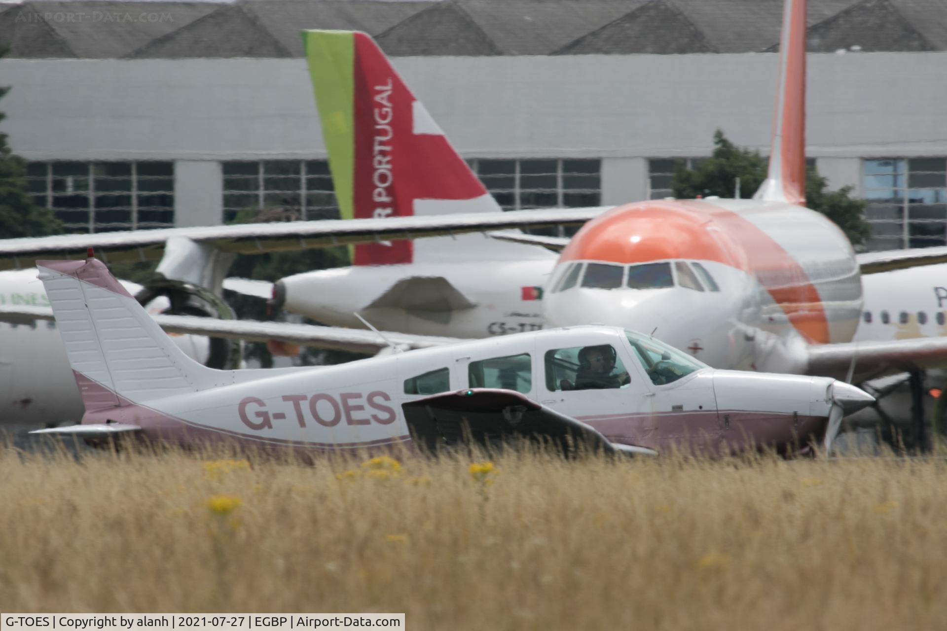 G-TOES, 1978 Piper PA-28-161 Cherokee Warrior II C/N 28-7816512, Rolling out behind the long grass and in front of stored airliners at Kemble / Cotswold Airport