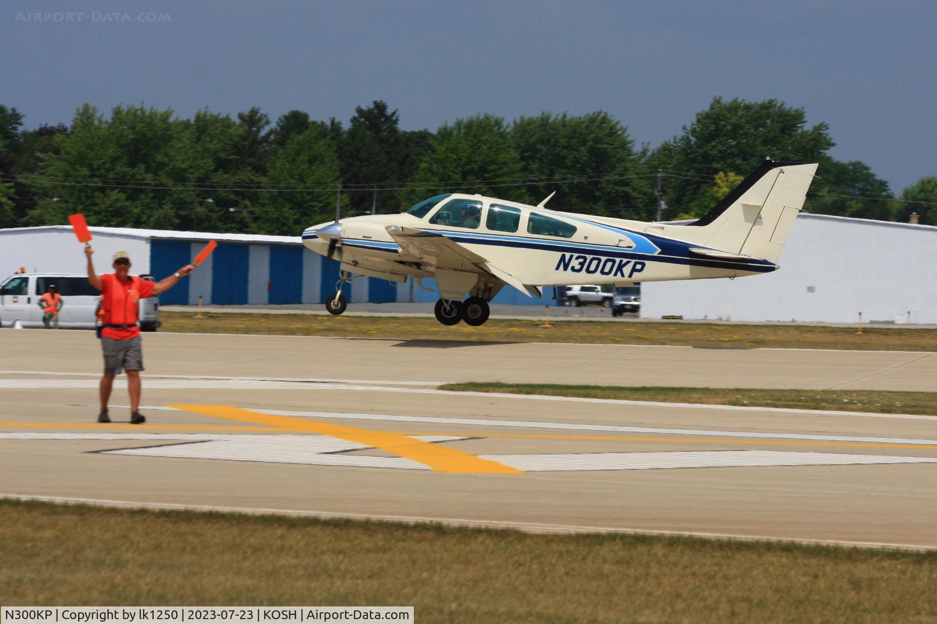 N300KP, 1979 Beech B-55 C/N TC-2240, While this Beech 55 Baron is landing for EAA AirVenture 2023 is a EAA volunteer busy to signal taxiing aircraft for another location on the field.