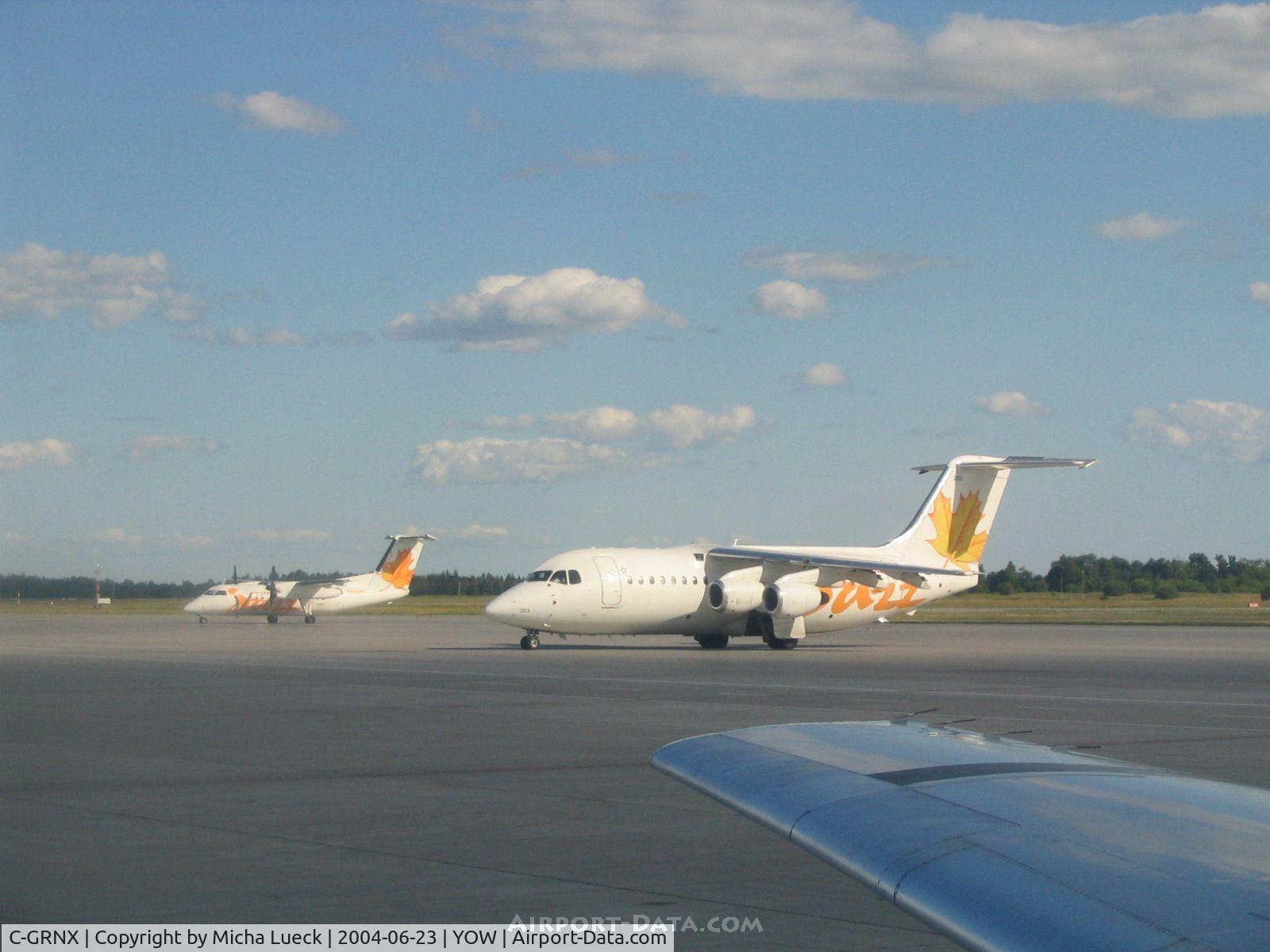 C-GRNX, 1989 British Aerospace BAe.146-200 C/N E2130, BAe 146 and Dash 8, both in the yellow Air Canada Jazz colour scheme, see over the wing of JetsGo's F100 C-GKZA