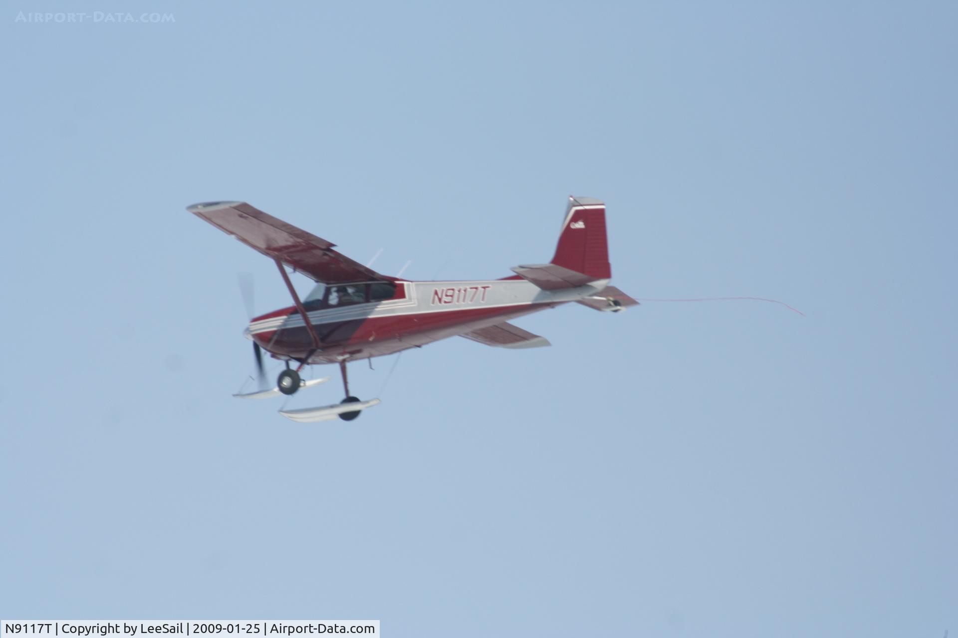 N9117T, 1959 Cessna 180B C/N 180-50617, Photo Taken of Plane Climbing Out over Forest Lake. Don't know what's with the rope trailing behind.