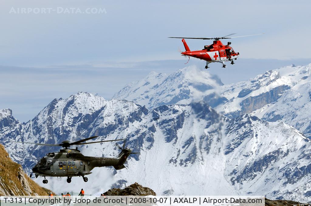 T-313, 1987 Aerospatiale Super Puma TH86 (AS-331M1) C/N 2226, Overview of the helicopter pad of the Swiss Axalp armament rage. White Super Puma T-313 arrives Rega A109K2 HB-XWH starts for its rescue display.