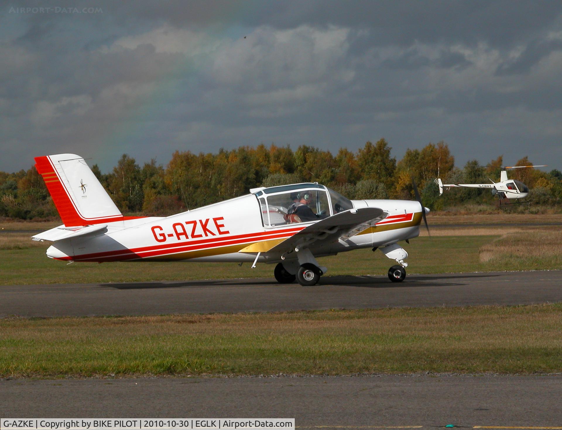 G-AZKE, 1972 Socata MS-880B Rallye Club C/N 1950, Rallye Club taxying past the cafe with R22 G-CBWZ manouvering behind