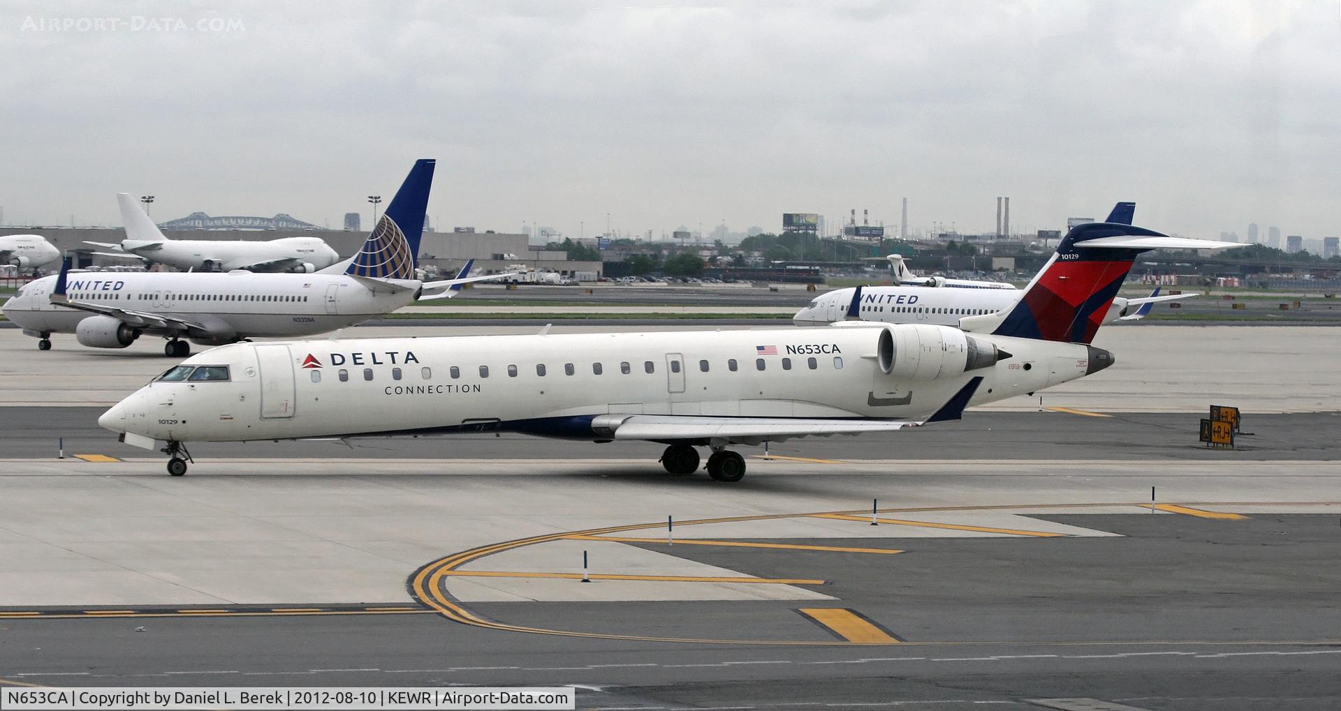 N653CA, 2003 Bombardier CRJ-700 (CL-600-2C10) Regional Jet C/N 10129, A Delta Connection CRJ taxies past chaos on Newark Liberty International's taxiways and runways caused by delays because of severe thunderstorms.