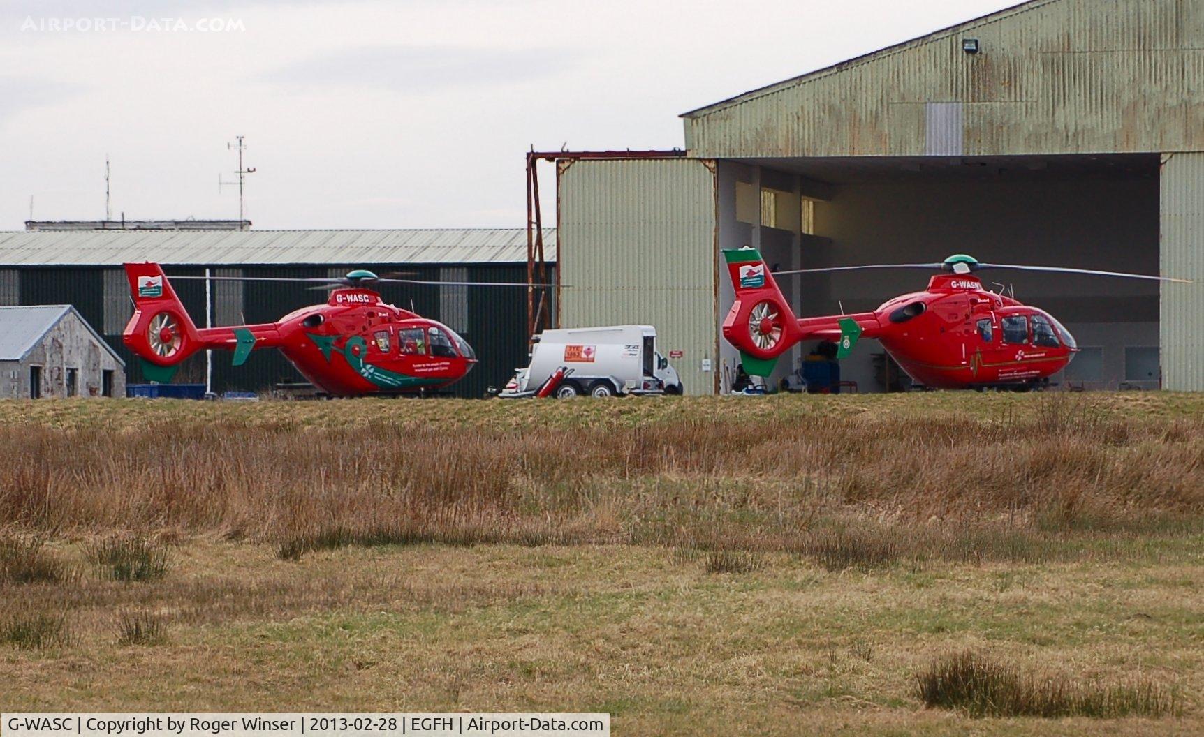 G-WASC, 2012 Eurocopter EC-135T-2+ C/N 1074, Welshpool Airport based Wales Air Ambulance helicopter Helimed 59 (on the left) joins resident Helimed 57 (G-WASN) at the South Wales air ambulance base on the day before the 12th anniversary of the Wales Air Ambulance Service being founded.