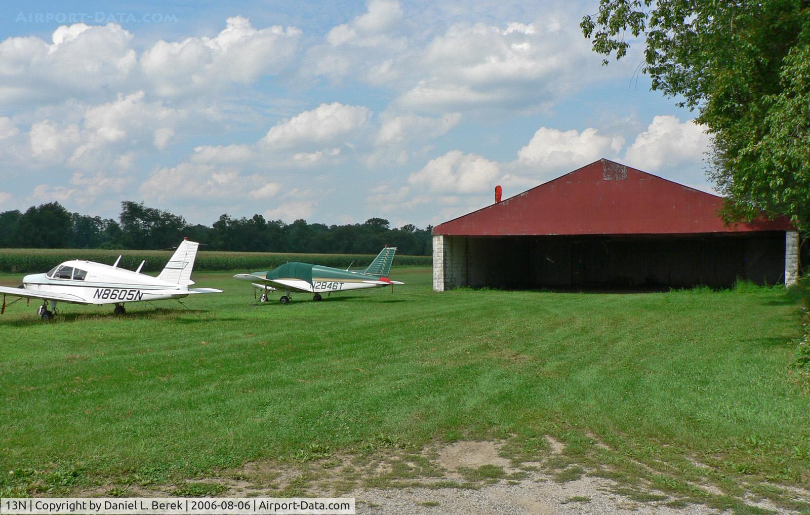 Trinca Airport (13N) - Two small planes sit on the apron by the hangar; the grass strip is in the background.