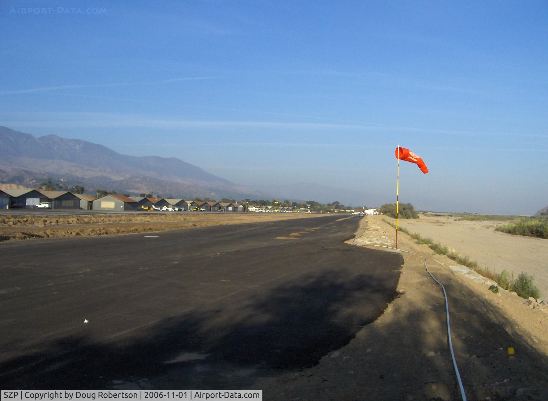 Santa Paula Airport (SZP) - New windsock at Runway 04 and new runway-parallel tiedown surfaced strip in preparation, the spaced clumps of dirt on the new surface show the bore holes for tiedown ring anchor insertions. Santa Clara River bed to the right