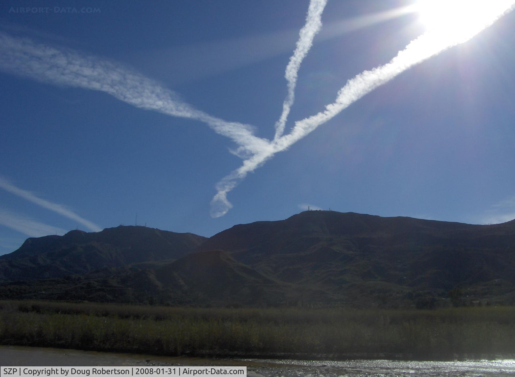 Santa Paula Airport (SZP) - Three jet contrails converging over Fillmore VORTAC FIM near SZP, South Mountain in background. Santa Clara River flowing from snowmelt and rain at base of photo.