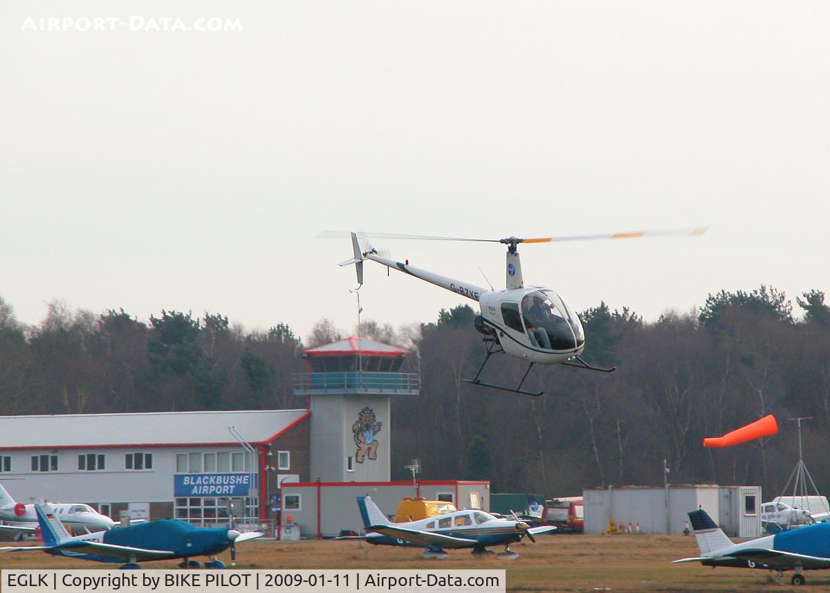 Blackbushe Airport, Camberley, England United Kingdom (EGLK) - LOOKING FROM THE AIRFIELD NORTH SIDE TOWARDS THE TERMINAL WITH ROLLASON R22 G-BZYE DEPARTING NORTH