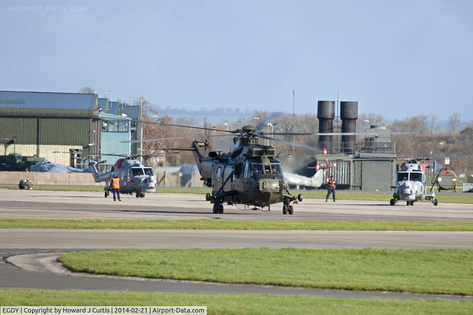 RNAS Yeovilton Airport, Yeovil, England United Kingdom (EGDY) - A view across the helicopter pan with several Lynx HMA8s and a Sea King HC4 heading out.  Visible behind are two stored Sea Harrier Fa2s and the FAA Museum to the left.