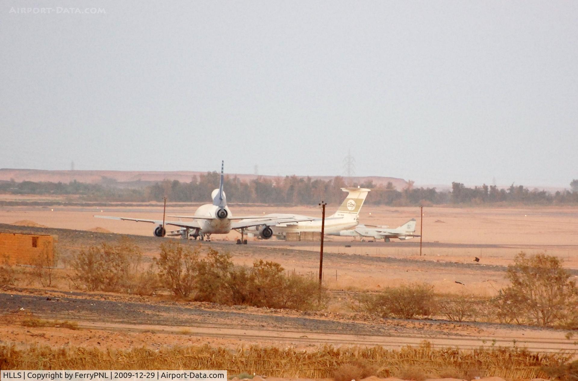 Sebha Airport, Sebha Libyan Arab Jamahiriya (HLLS) - Remote stand with stored L1011 of Kallat El-Saker Air Company (one of three), a Il76 of LAA and a MIG29. View from hotel.