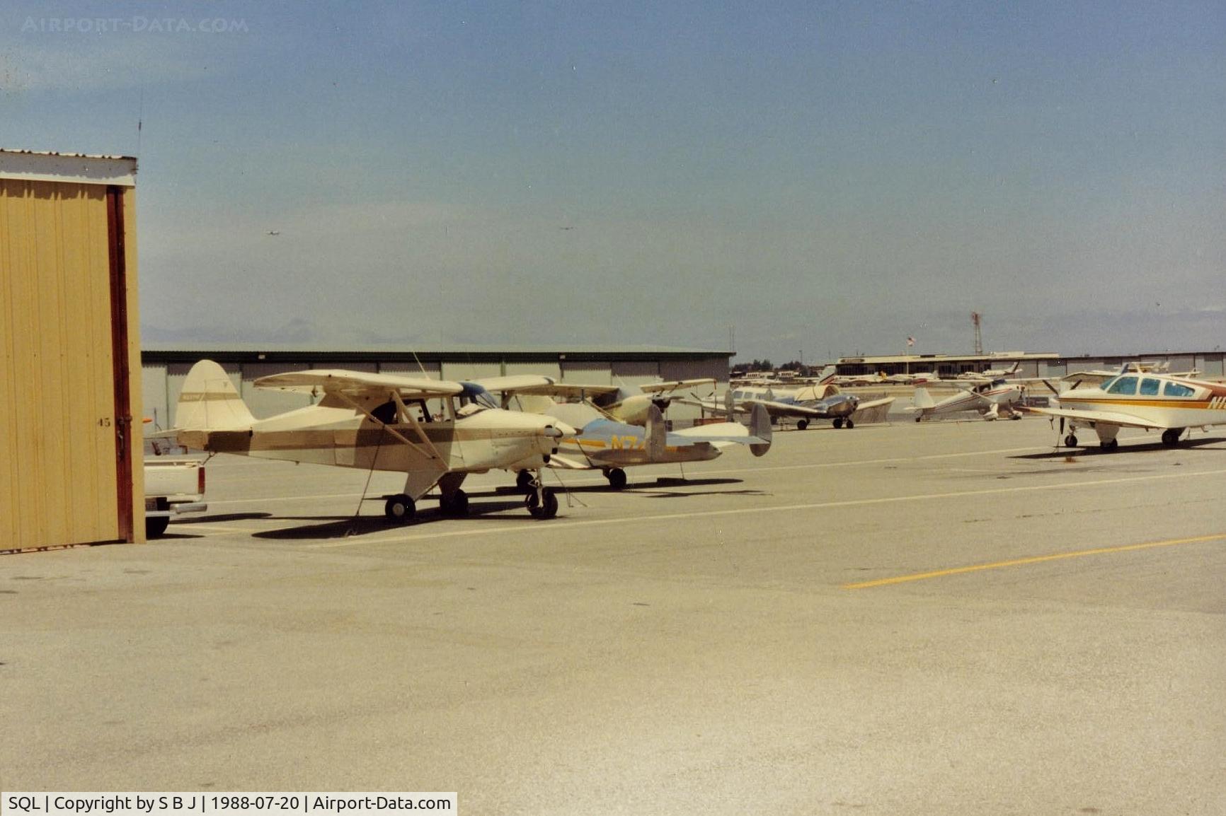 San Carlos Airport (SQL) - N2371P at San Carlos in 1988.View is  north and the administration building (flag) and  Sky Kitchen. Notice two airliners above 71P on (short) final to SFO.Was interesting flying under them (tower gave advisorys) when departing to the east.