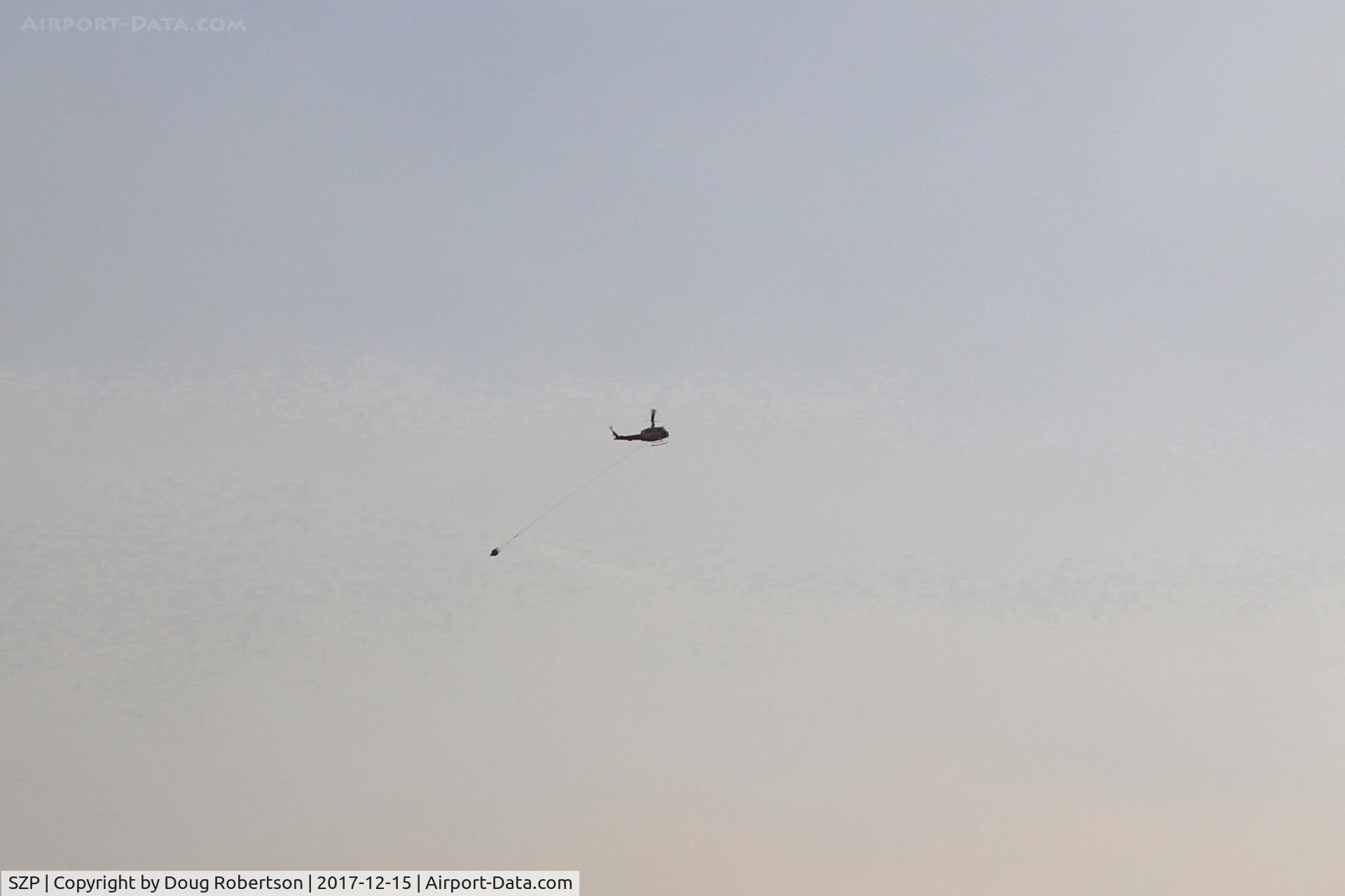 Santa Paula Airport (SZP) - Firebomber with sling load of dumped retardant returning to SZP. The Thomas Aquinas College, Steckel Park & Santa Paula Hospital have been evacuated. Highway 150 closed date of photo. Please view large.