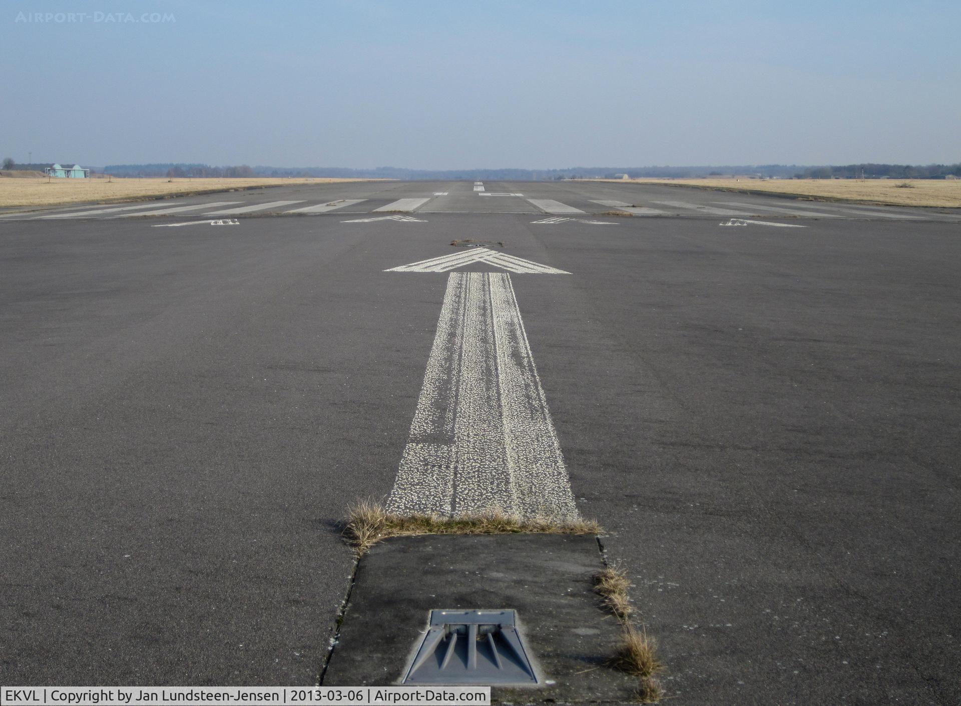 EKVL Airport - Arrow pointing to the displaced threshold of Runway 10 at the closed Vaerloese Air Base in Denmark. In the foreground a white approach light.