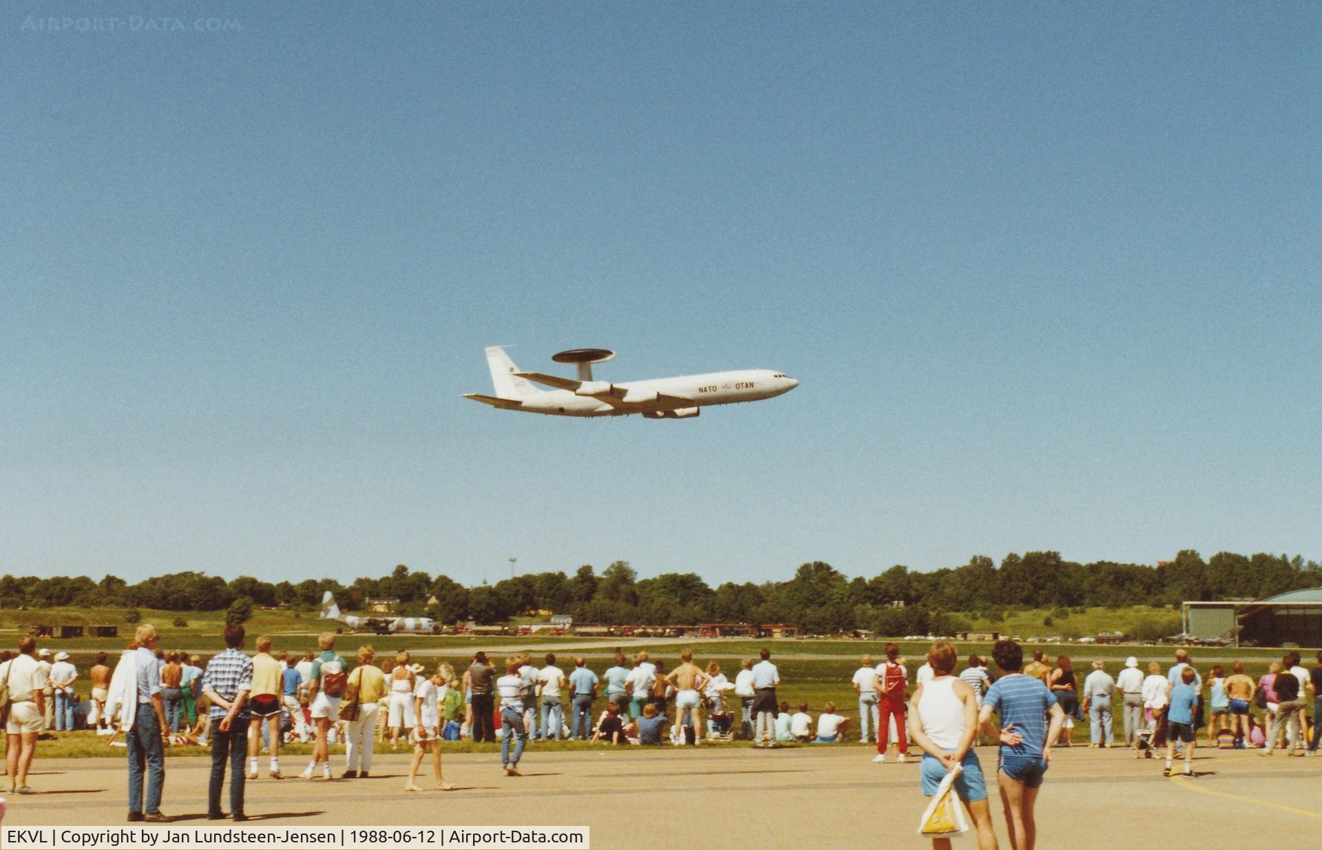 EKVL Airport - NATO Boeing E-3A Sentry 90449 flying over Runway 10 at Vaerloese Air Base Open House 1988 in Denmark. In background left to right: RAF C-130K, RAF Red Arrows Hawks being refueled, RAF Harrier and German Tornado side by side at hangar.